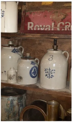 Blue-decorated stoneware jugs beside an old Royal Crown sign